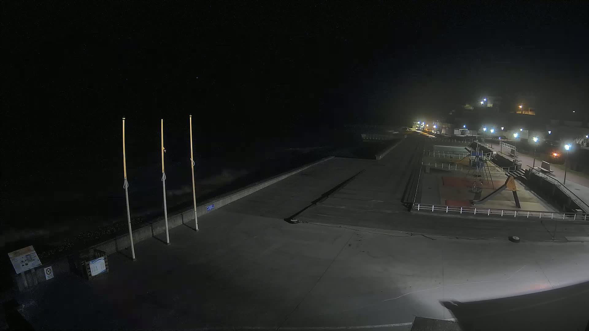 A nighttime view of an empty seaside promenade with a playground and a partly cloudy sky.