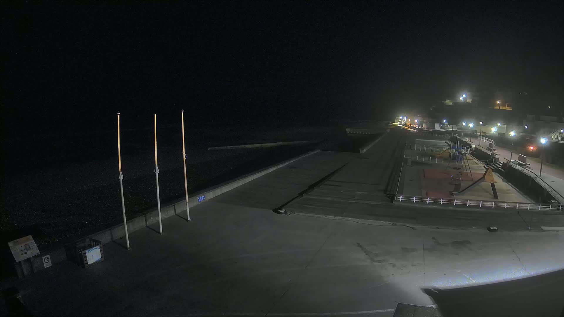 A nighttime view of an empty seaside promenade with a playground and a few lights, under foggy conditions.