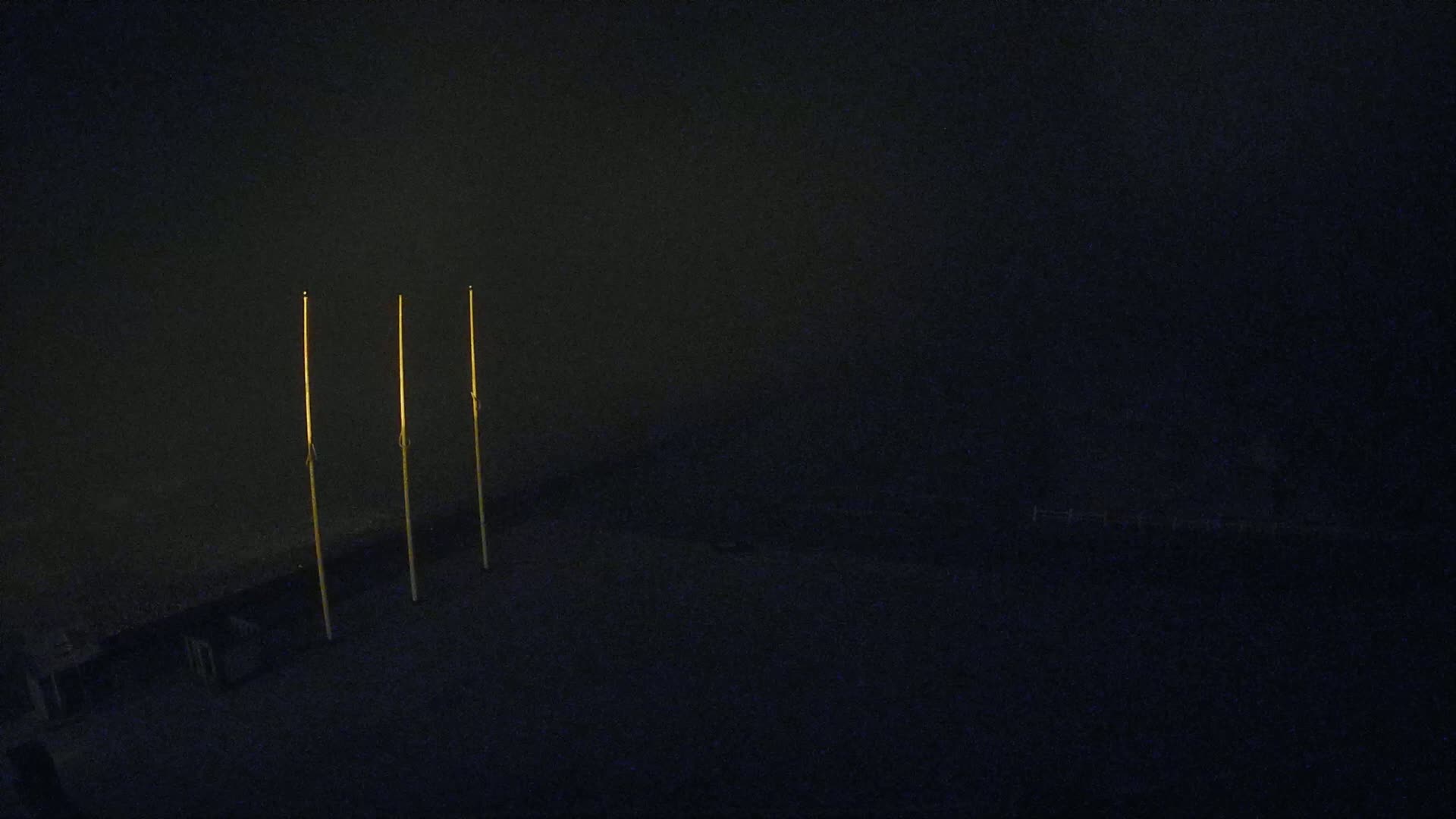 Three tall, slender poles stand upright against a dark, nighttime background.