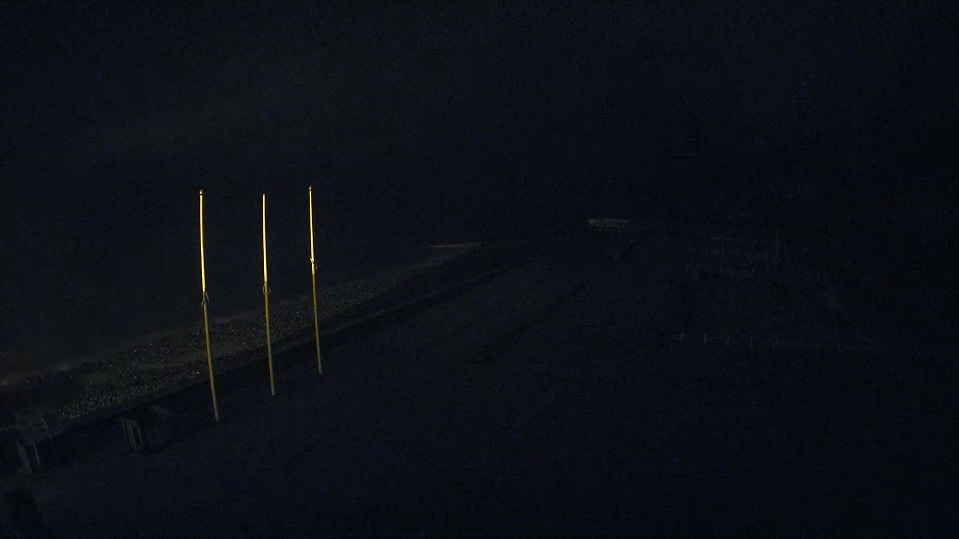 Three tall, thin, illuminated poles stand on a dark, sloped surface at night.