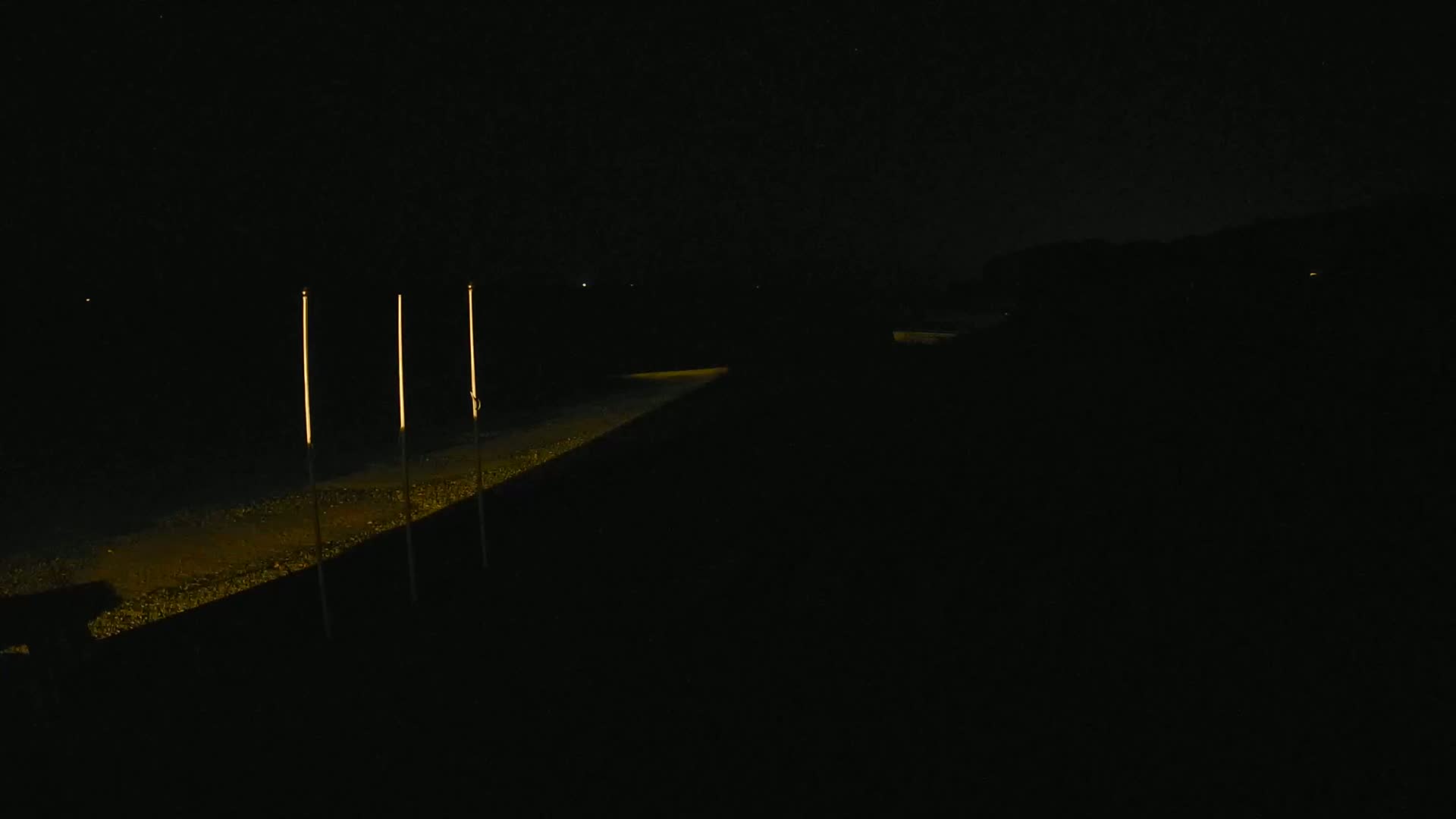 Three tall, slender lights illuminate a dark path at night.