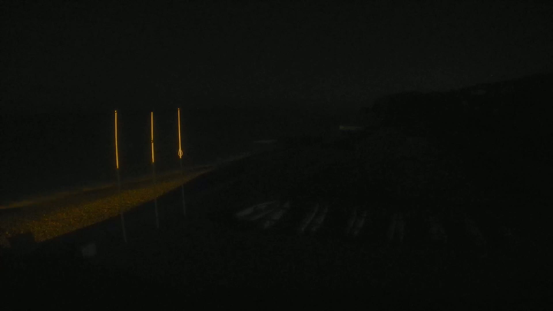 Three tall, slender lights illuminate a dark, sandy beach at night.