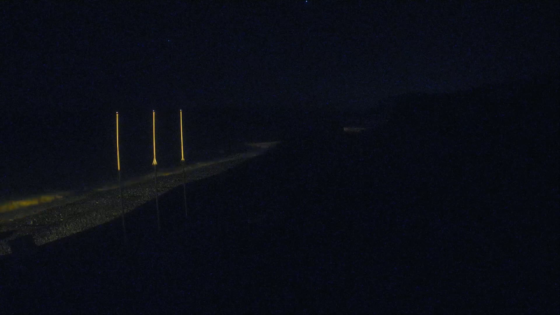 Three tall, slender lights illuminate a dark, nighttime landscape.