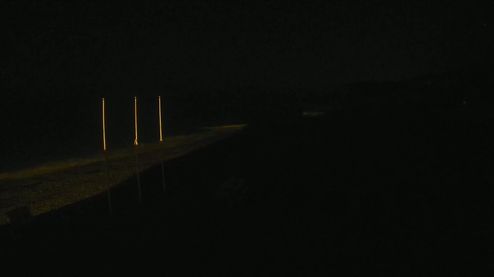 Three tall, slender lights illuminate a dark beach at night.