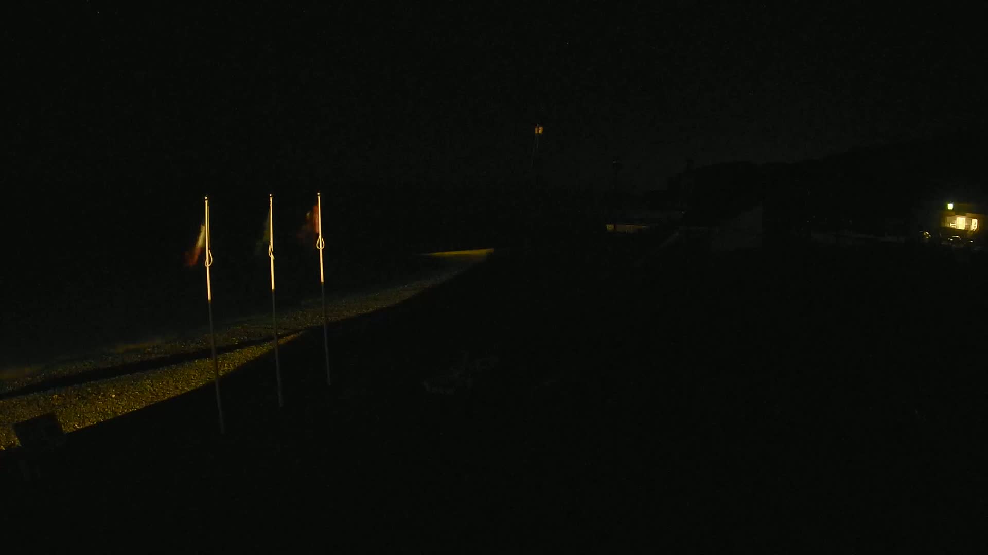 Three flags are illuminated on a dark beach at night.
