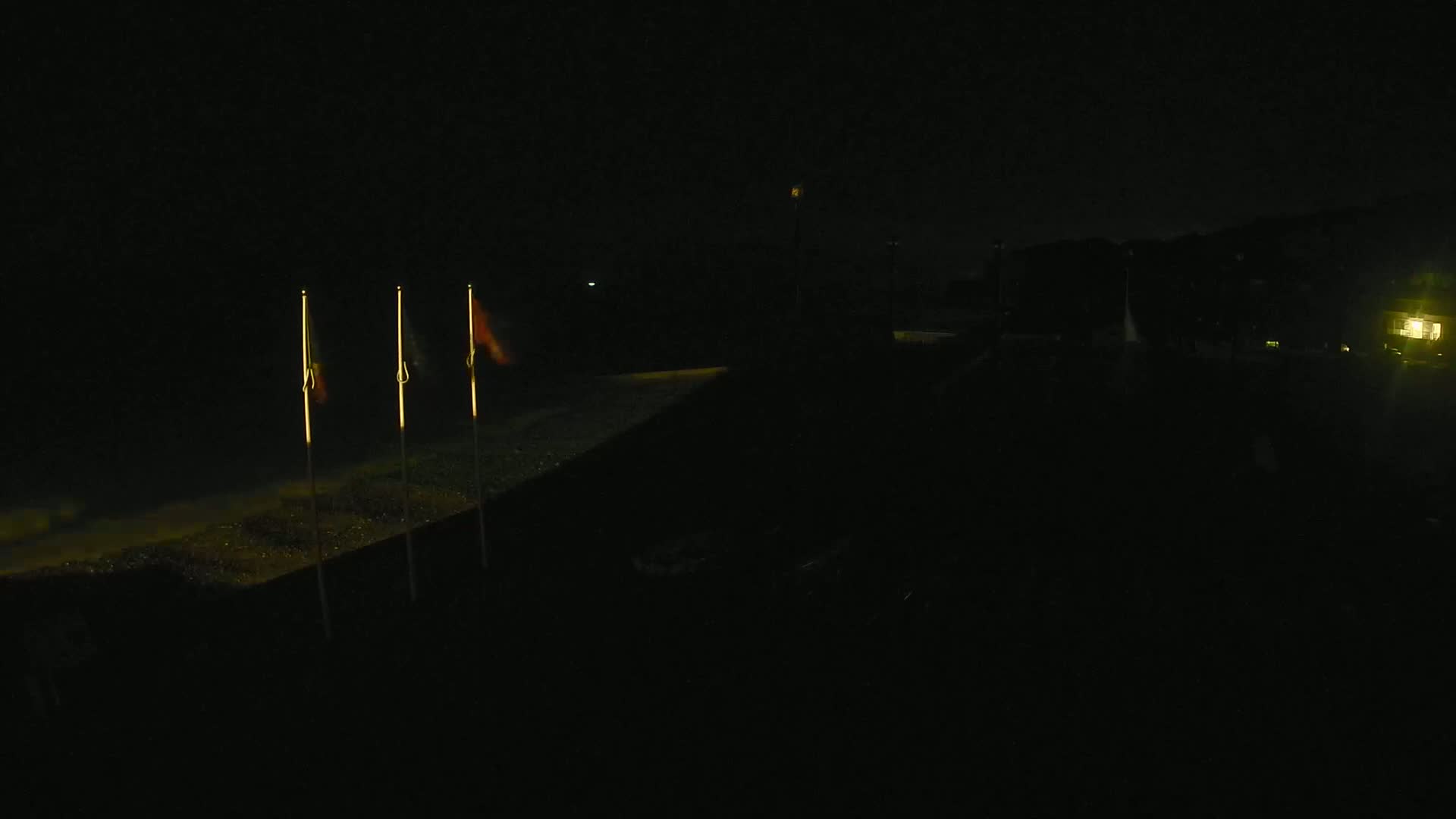 Three illuminated flags stand on a dark, possibly grassy, area at night.