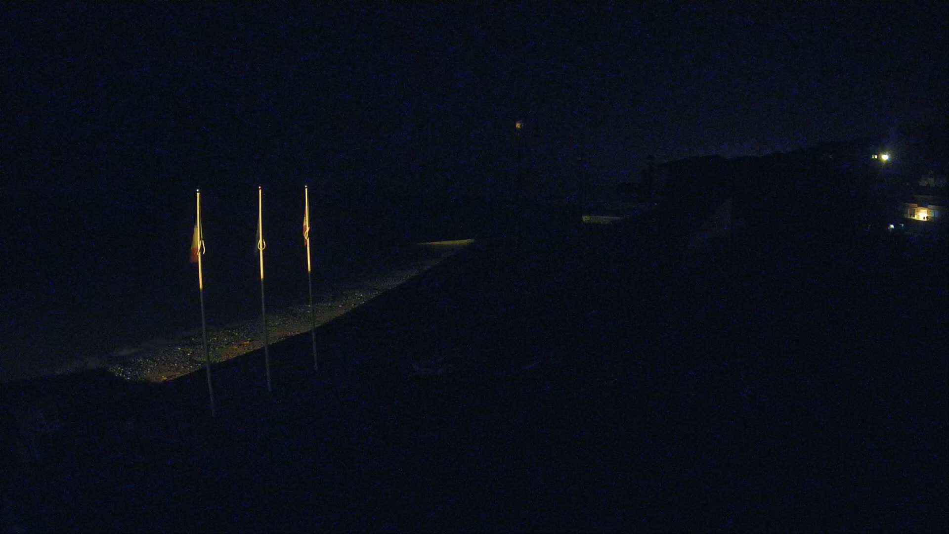 Three dimly lit flags stand on a dark, sloped surface at night.