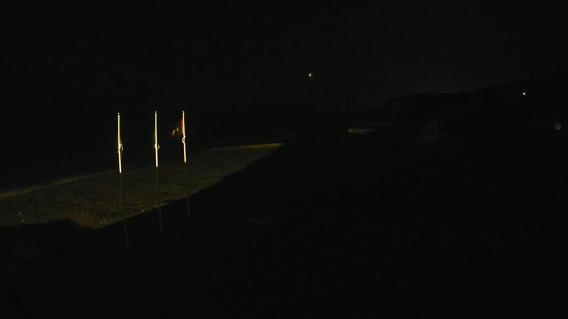 Three illuminated poles stand on a dark, possibly paved surface at night.