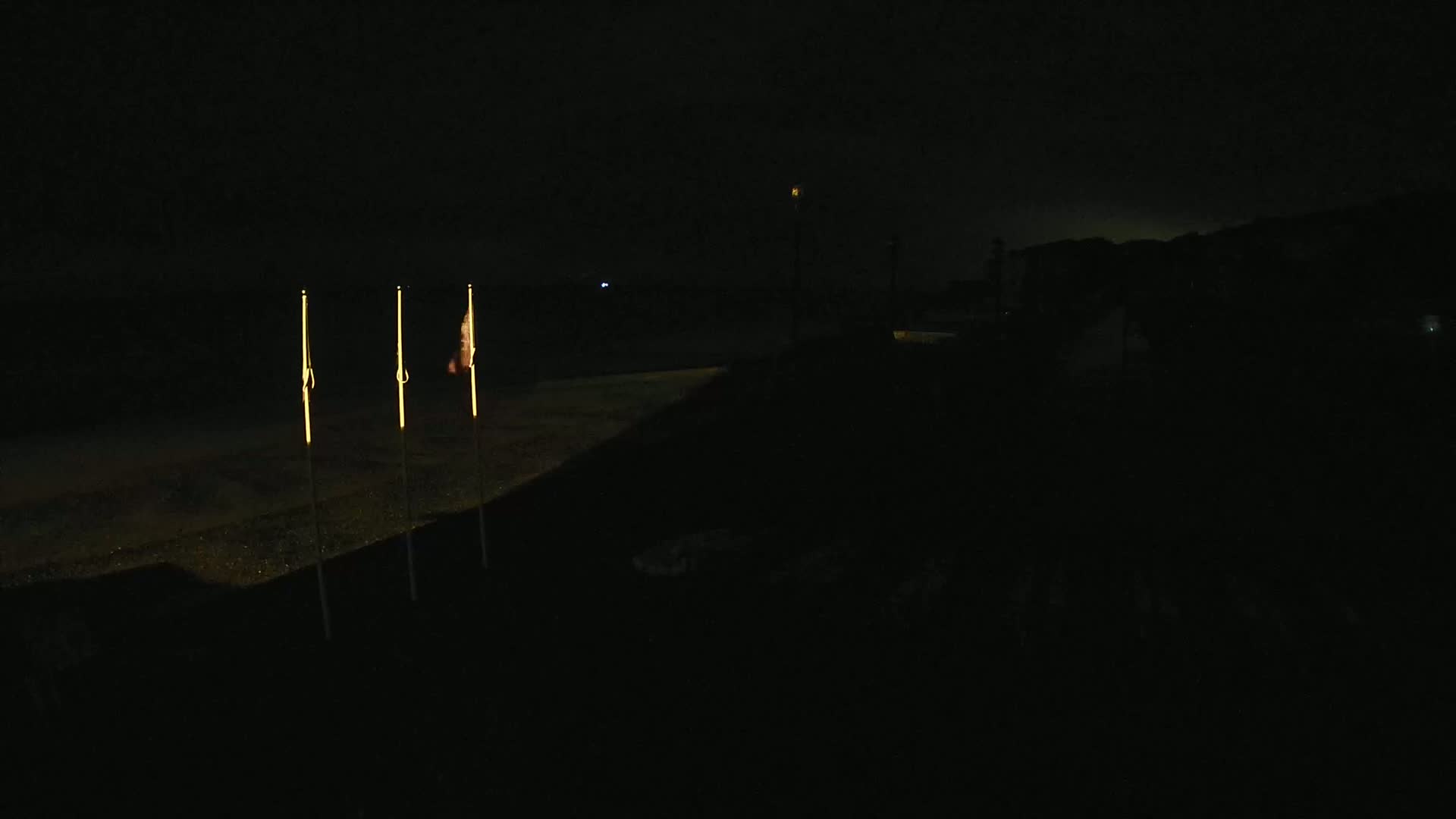 Three illuminated flagpoles stand on a dark, flat surface at night.