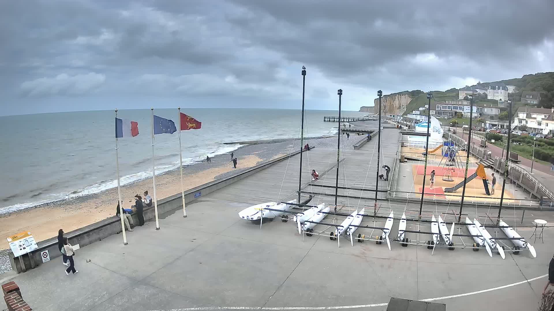 A beach with several small sailboats on land, a playground, and a pier under a cloudy sky.