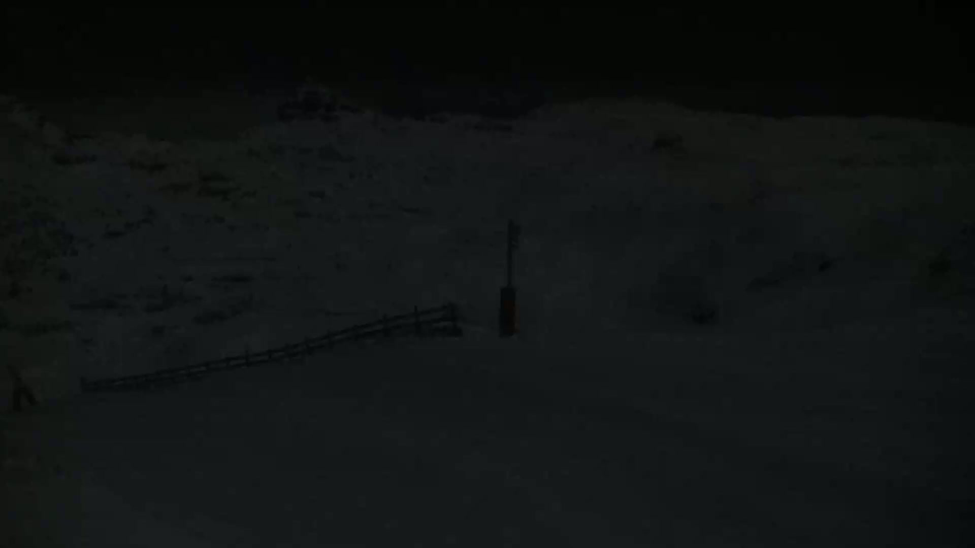 A snow-covered landscape at night is visible, featuring a short fence and a dark post.