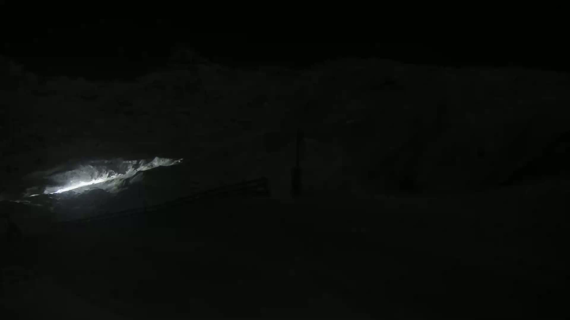 A sliver of bright light illuminates a dark, snowy landscape at night.
