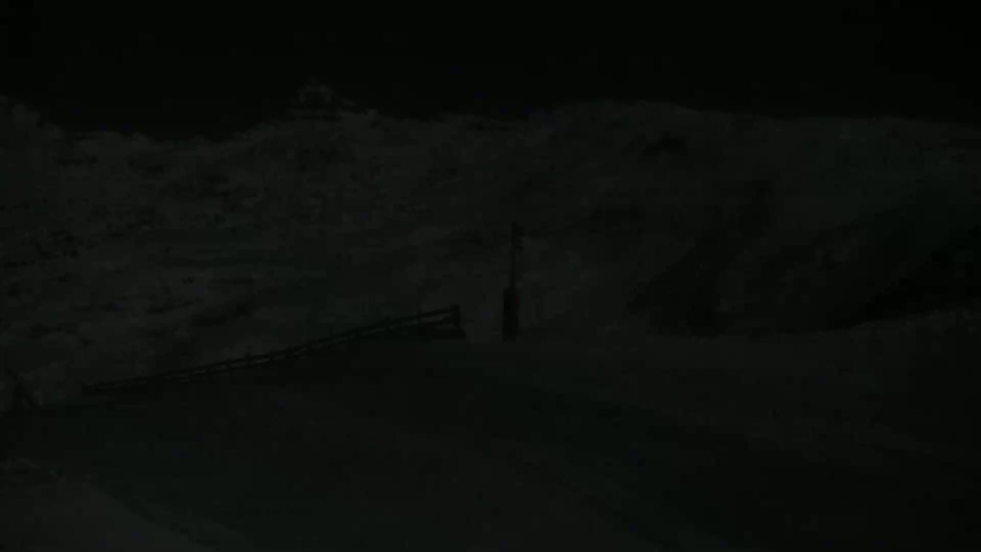A dark, snowy landscape is visible at night, with a portion of a railing or fence in the foreground.