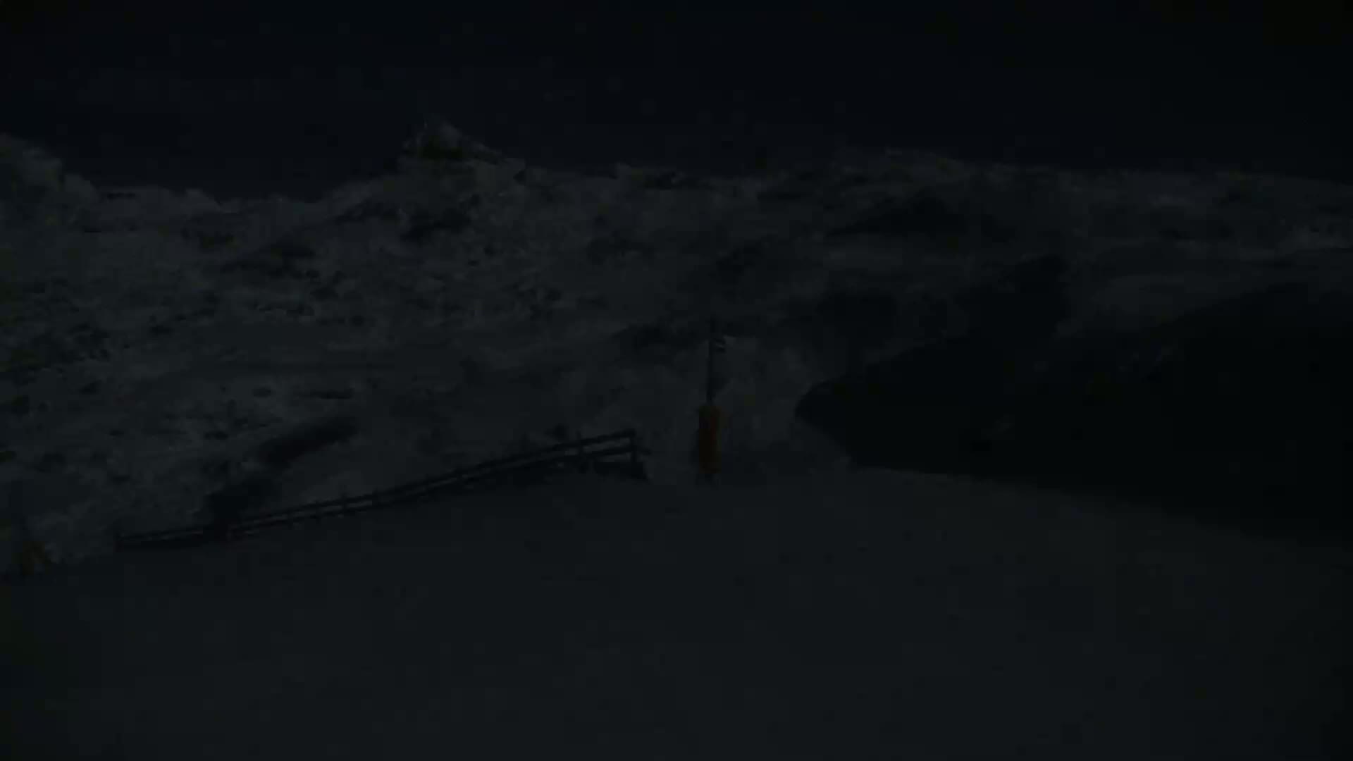 A snow-covered landscape is visible at night, with a low fence and a lone post in the foreground.