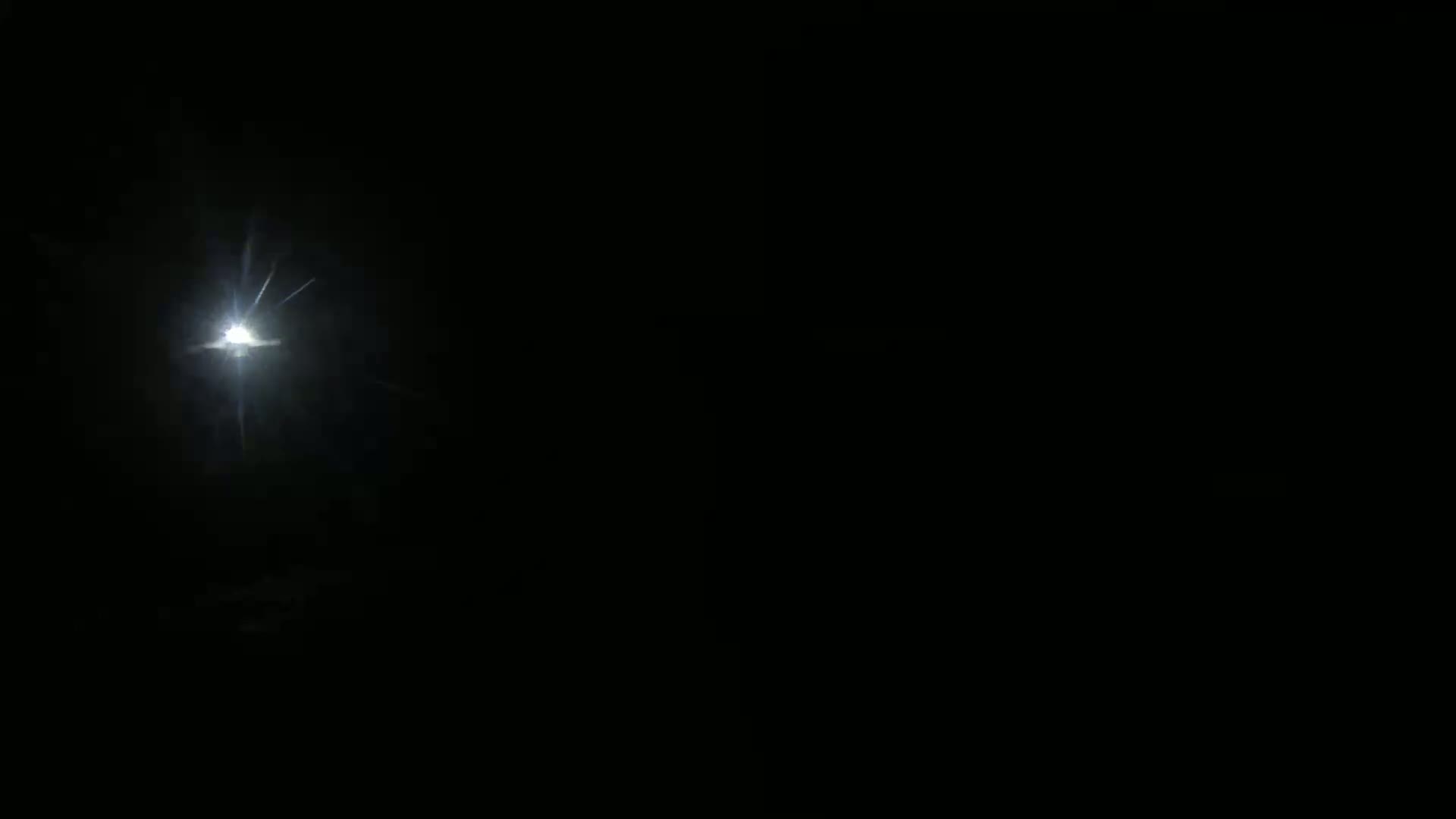 A bright light, possibly a streetlight or a distant star, shines through a dark, nighttime sky.