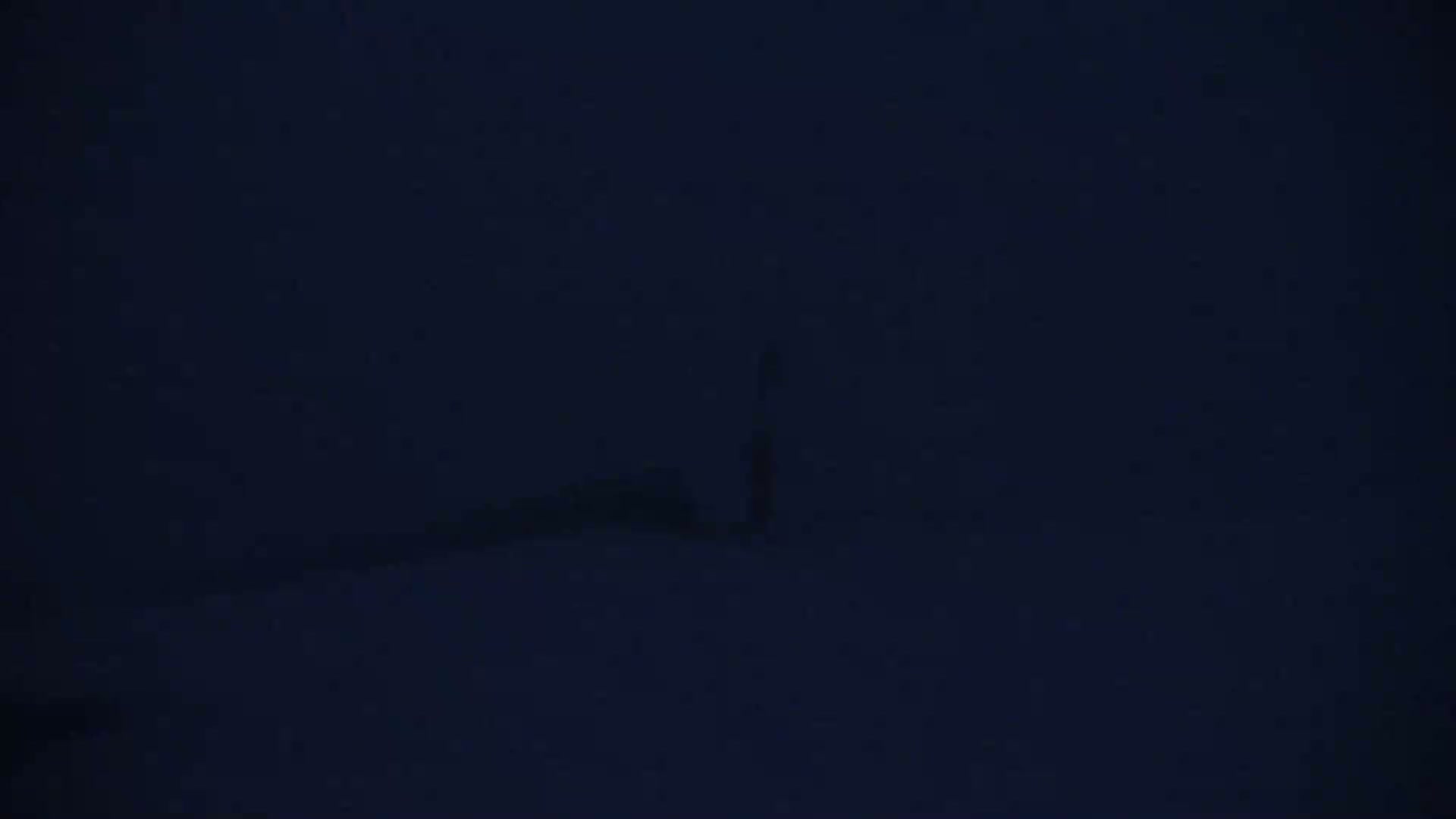 A dark, blurry figure stands in the distance on a snow-covered landscape under a dark night sky.