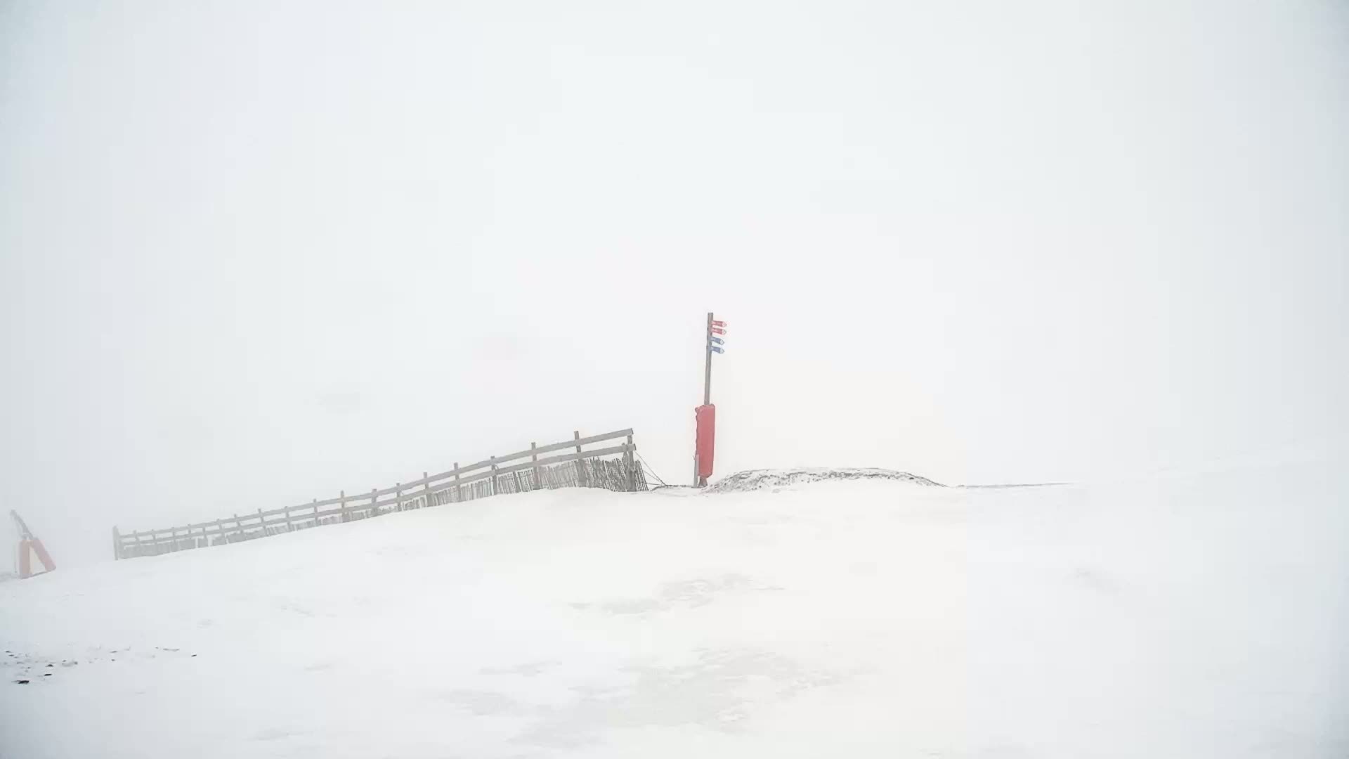 A snow-covered landscape with a wooden fence and a flagpole in foggy conditions.