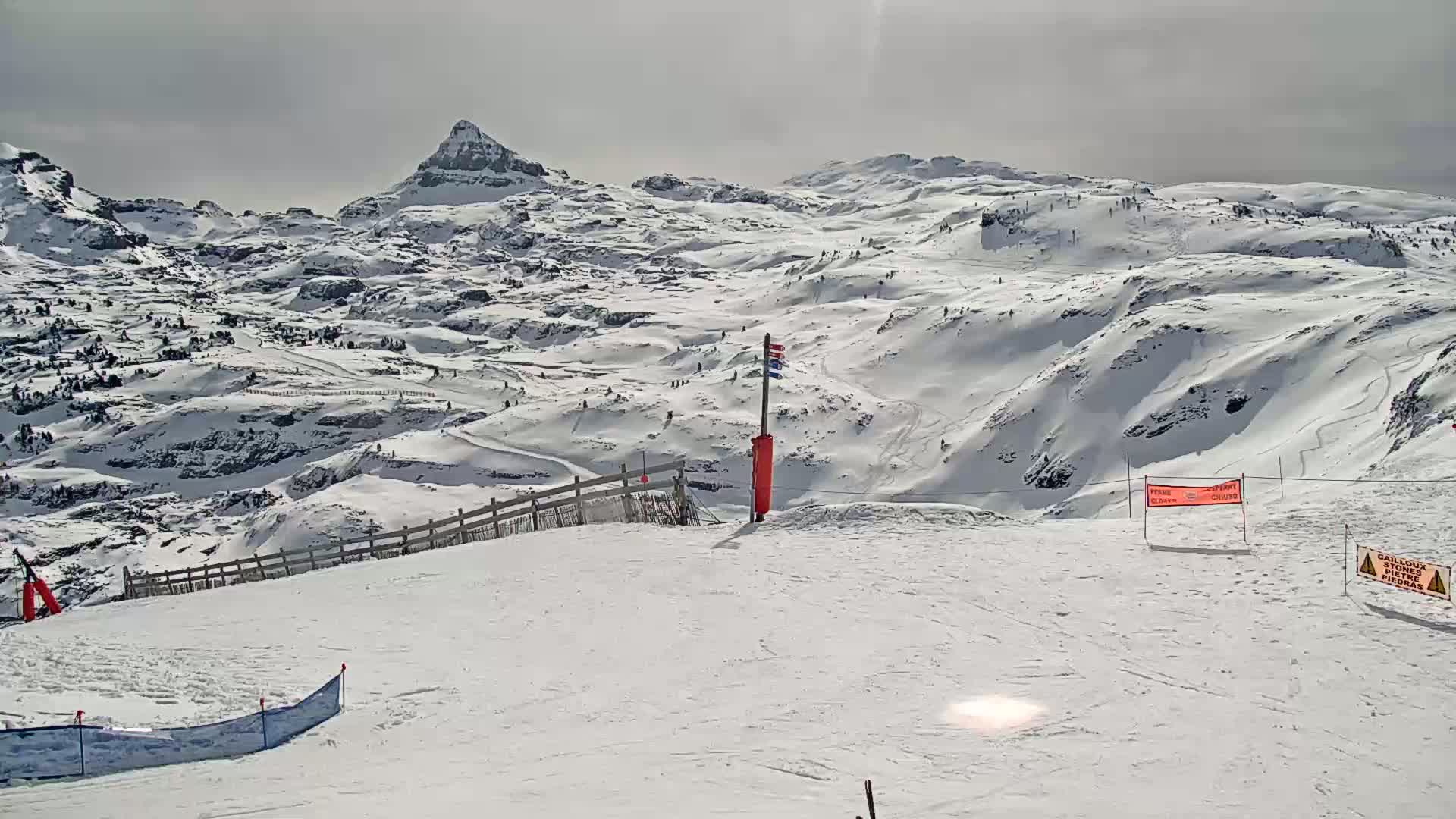 A snow-covered mountain range with ski slopes under a mostly cloudy sky.