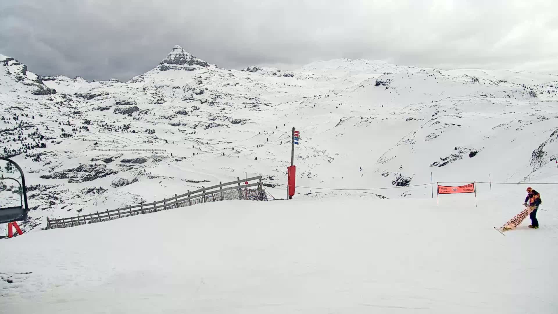 A snow-covered mountain landscape under an overcast sky, with a person carrying a snowboard near a ski lift.
