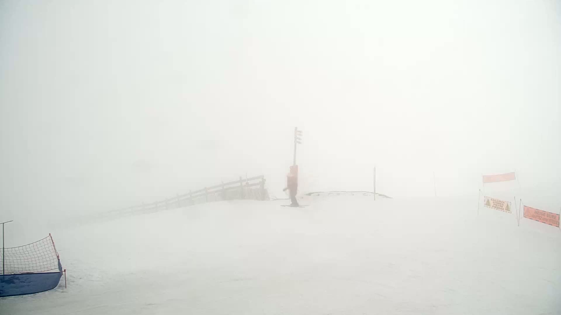 A lone figure skis down a snow-covered slope shrouded in thick fog.