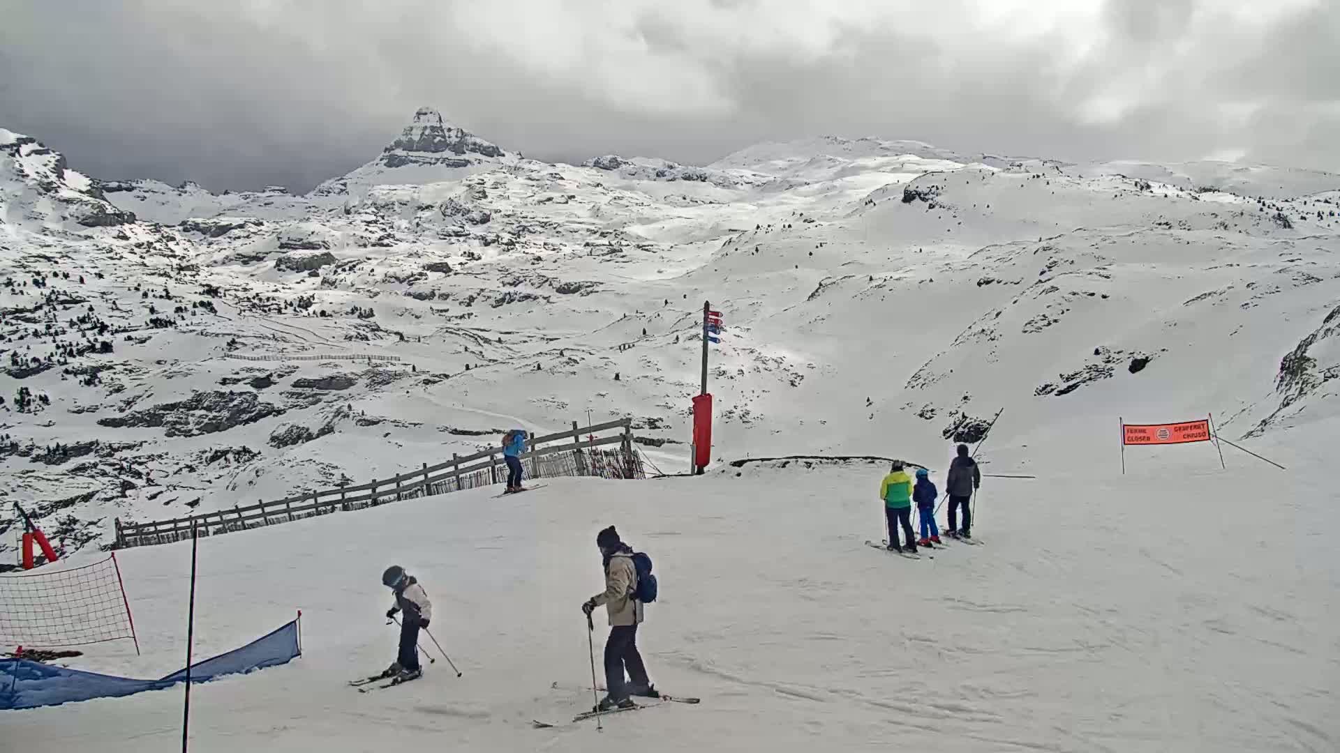 A snow-covered mountain landscape with several skiers on a slope under an overcast sky.