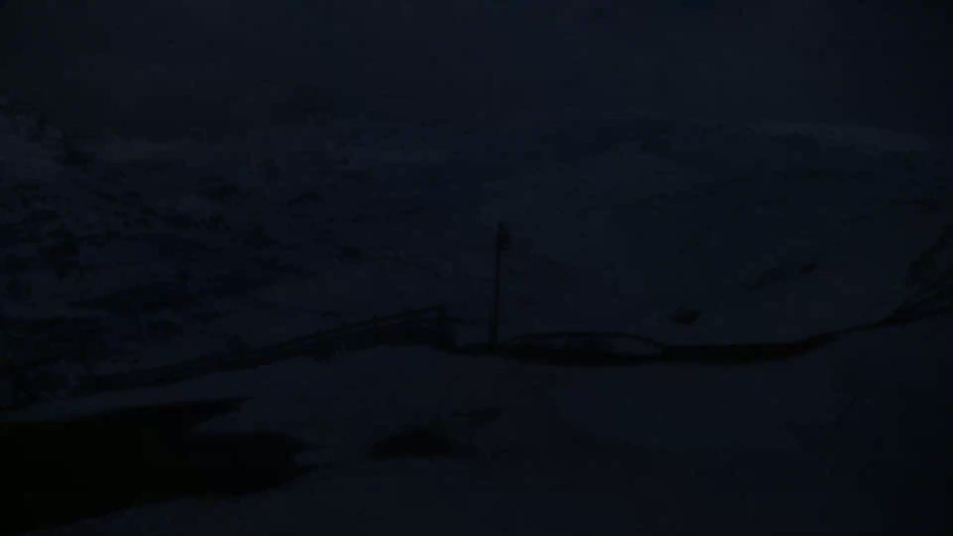 A dark, snowy landscape is visible at night, with a lone pole standing in the middle ground.