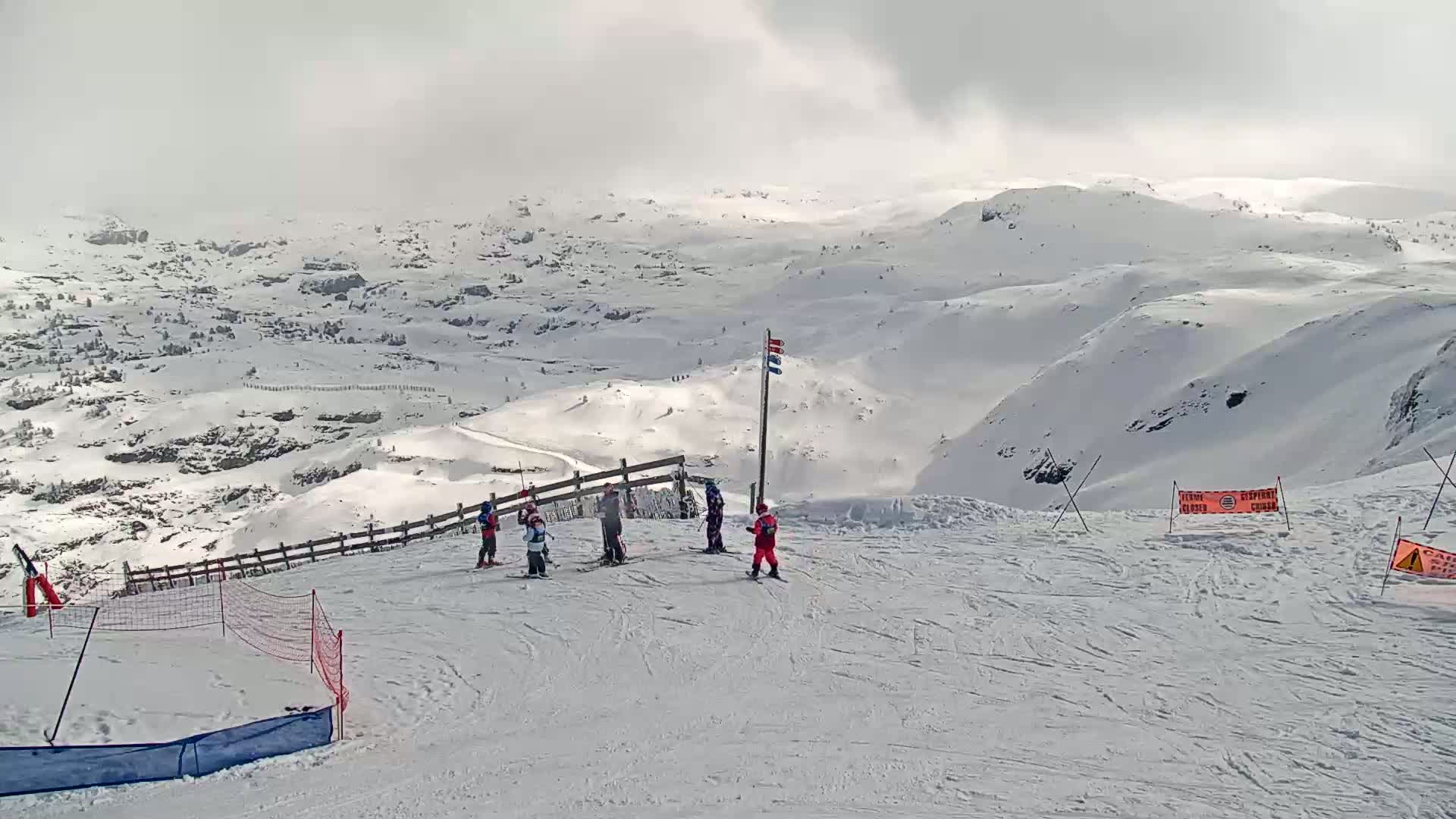 A snowy mountain landscape with several skiers on a slope under an overcast sky.