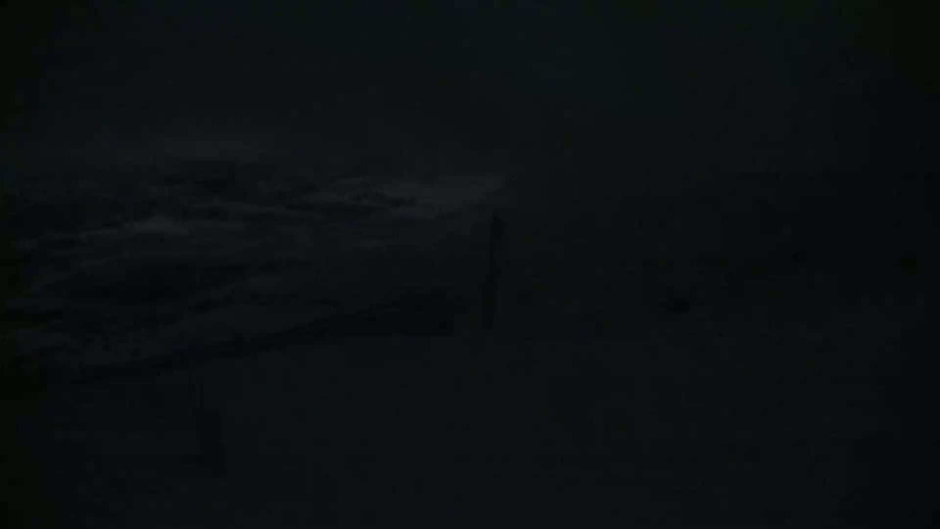 A dark, nighttime scene shows a mostly obscured landscape under a cloudy sky.