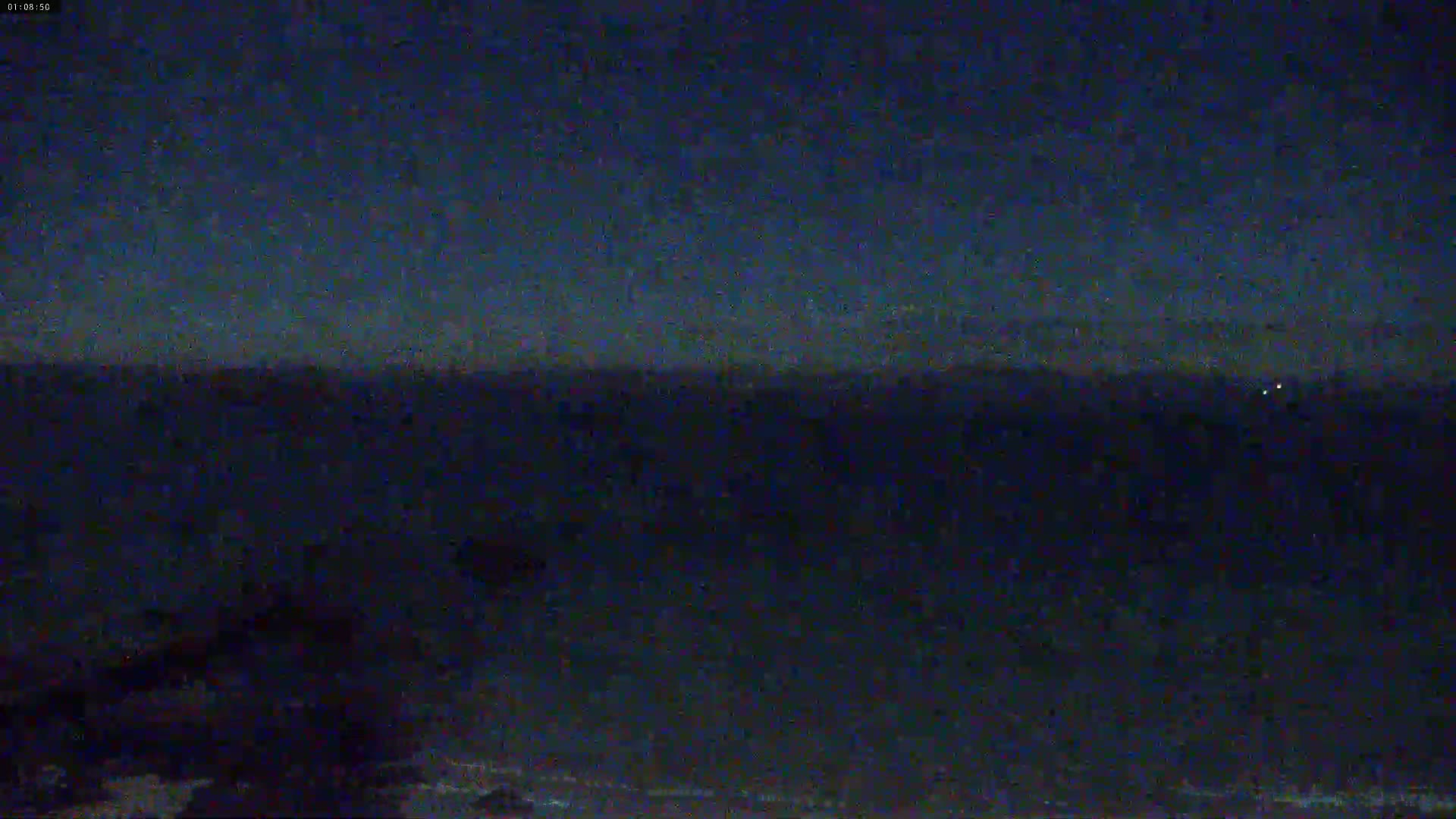 A dark, nighttime landscape shows a distant horizon under a clear, dark blue sky.