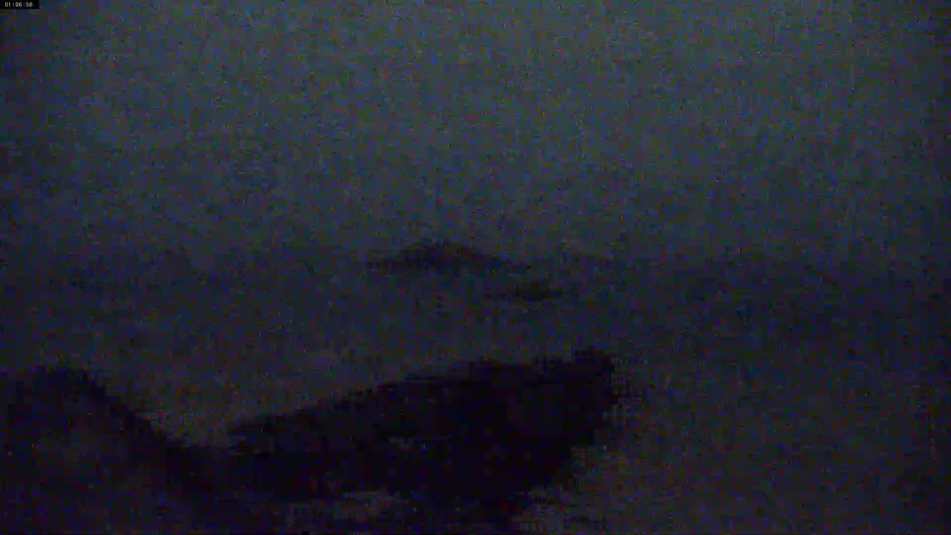 A dark, blurry image shows indistinct shapes in the distance possibly representing land or hills under a nighttime sky.