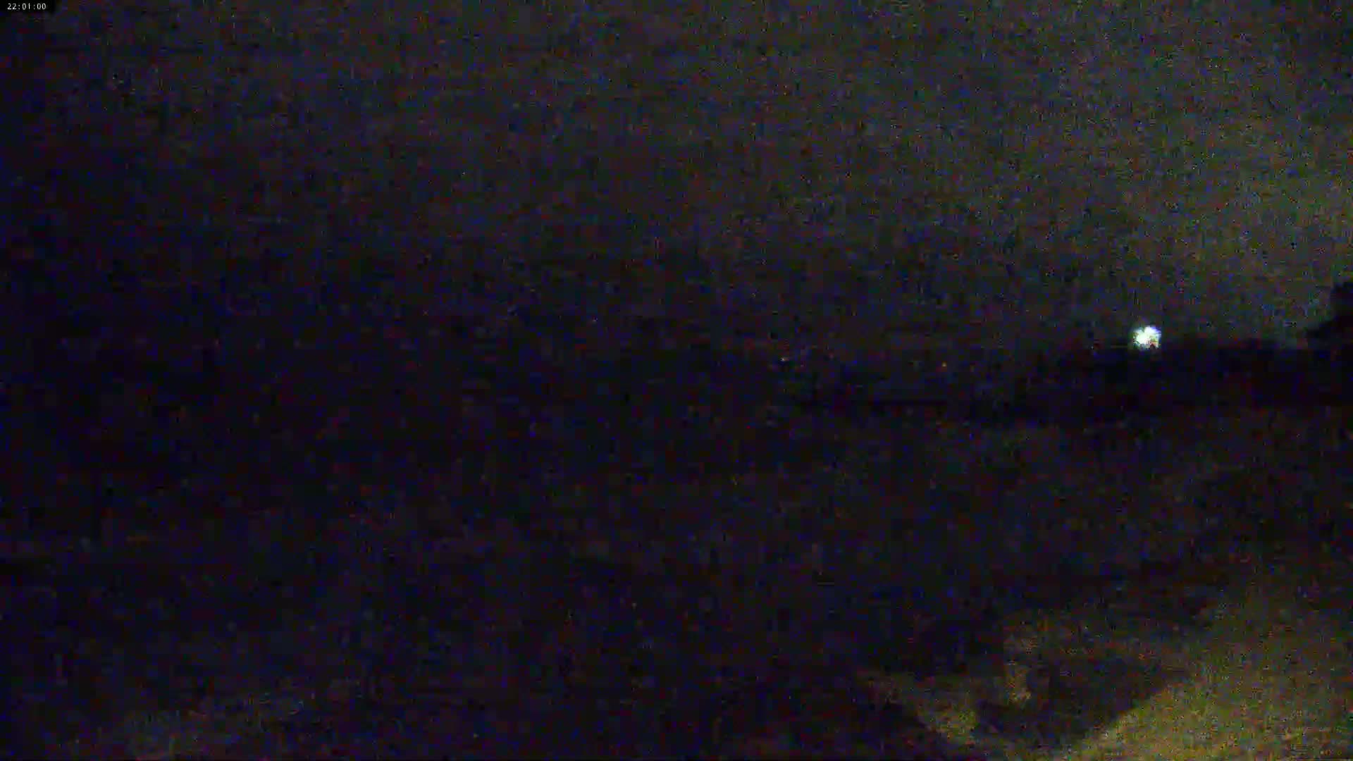 A dark, nighttime scene shows a dimly lit area, possibly outdoors, under a cloudy sky.