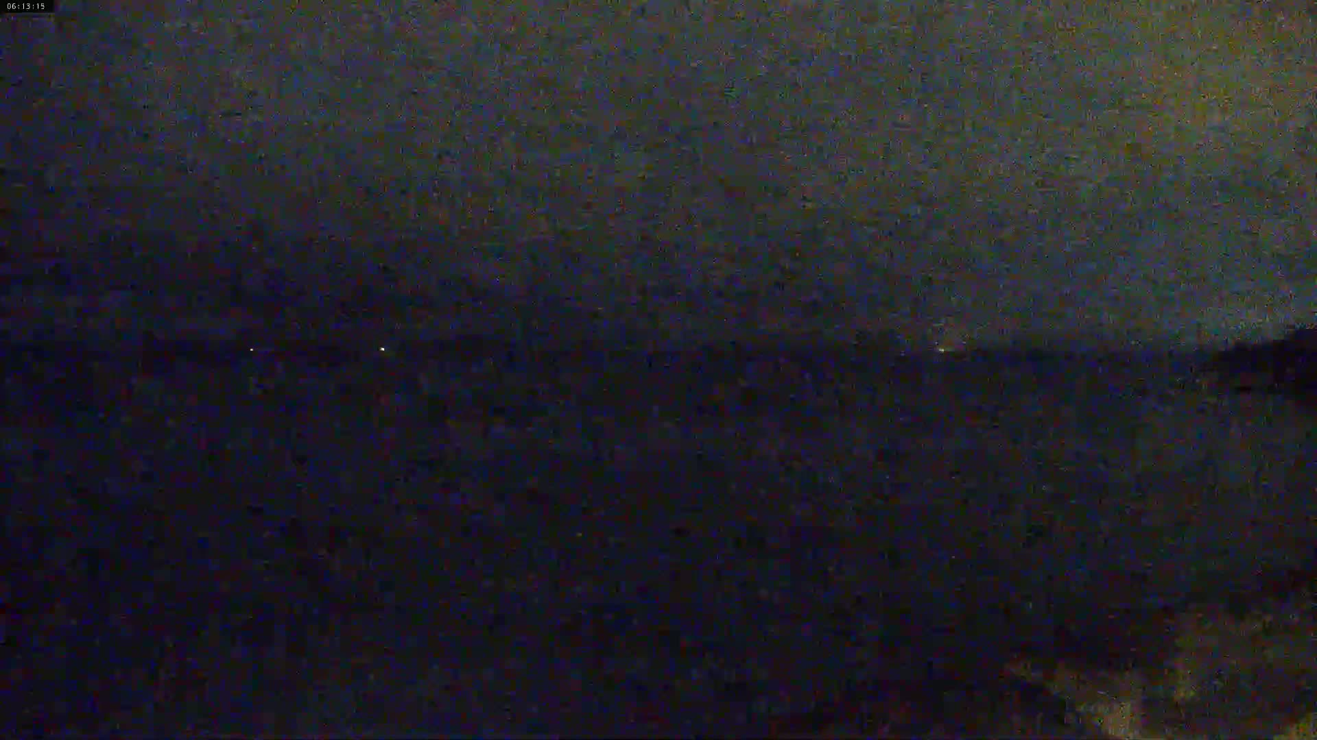 A dark, nighttime view of a body of water under a cloudy sky shows a few distant lights on the horizon.