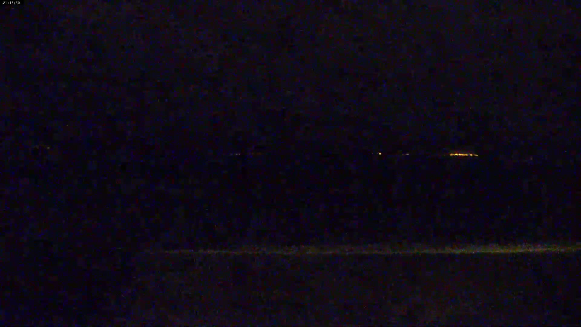 A dark nighttime scene shows a distant line of faint lights on the horizon.