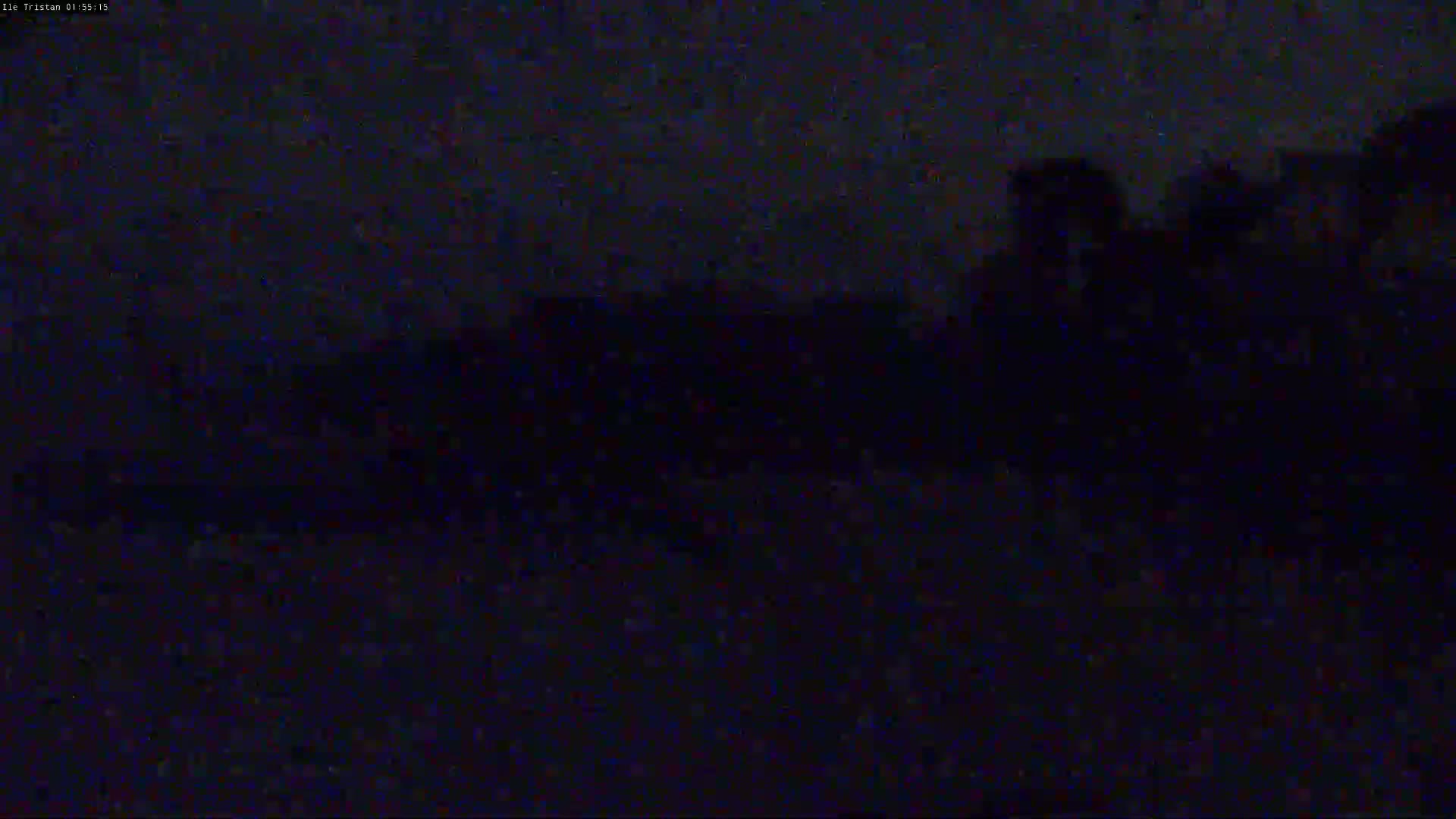 A dark, nighttime scene shows a blurry, indistinct landscape under a mostly clear, dark sky.