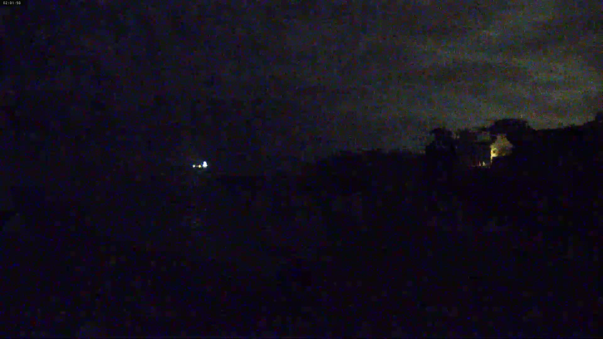 A dark, nighttime scene shows a distant light source and a silhouetted landscape under a cloudy sky.