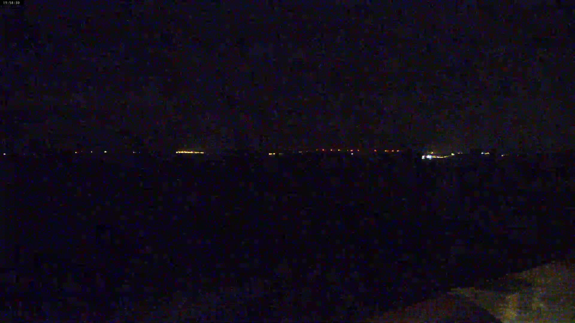A nighttime view shows a distant line of lights on the horizon under a dark, clear sky.