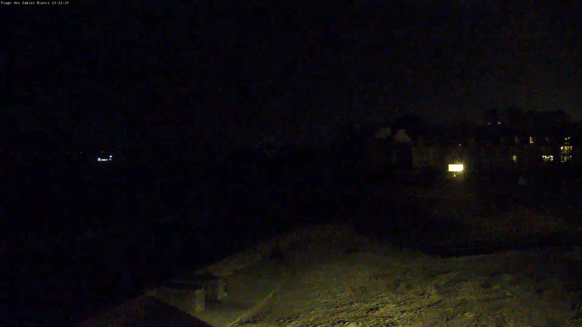 A nighttime view shows dimly lit buildings in the distance and a dark, textured foreground under a clear, dark sky.