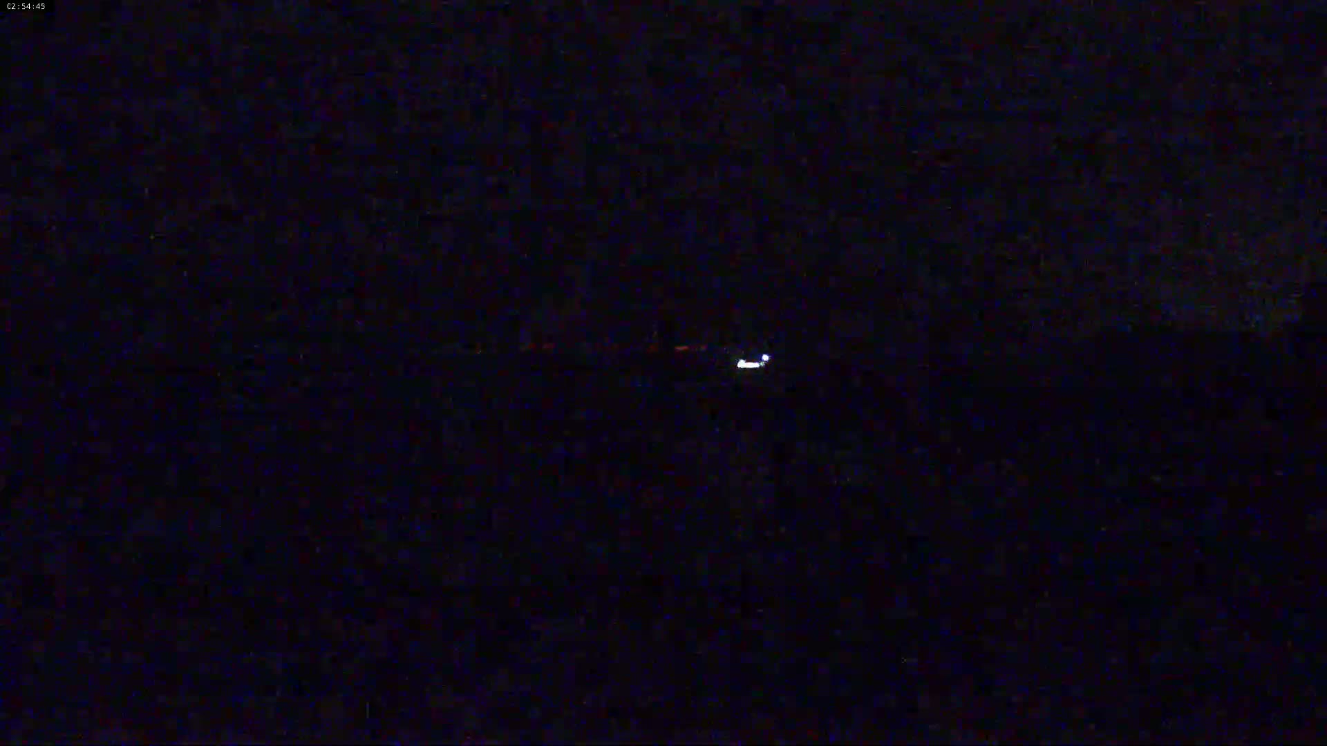 A single, small, bright light is visible in the distance on a dark, nighttime landscape.