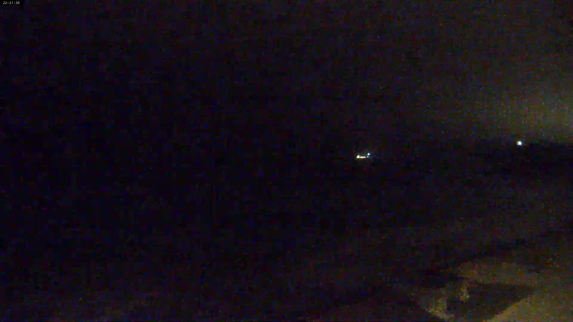 A dark, nighttime scene shows a few distant lights on a flat, dark landscape under a clear, dark sky.