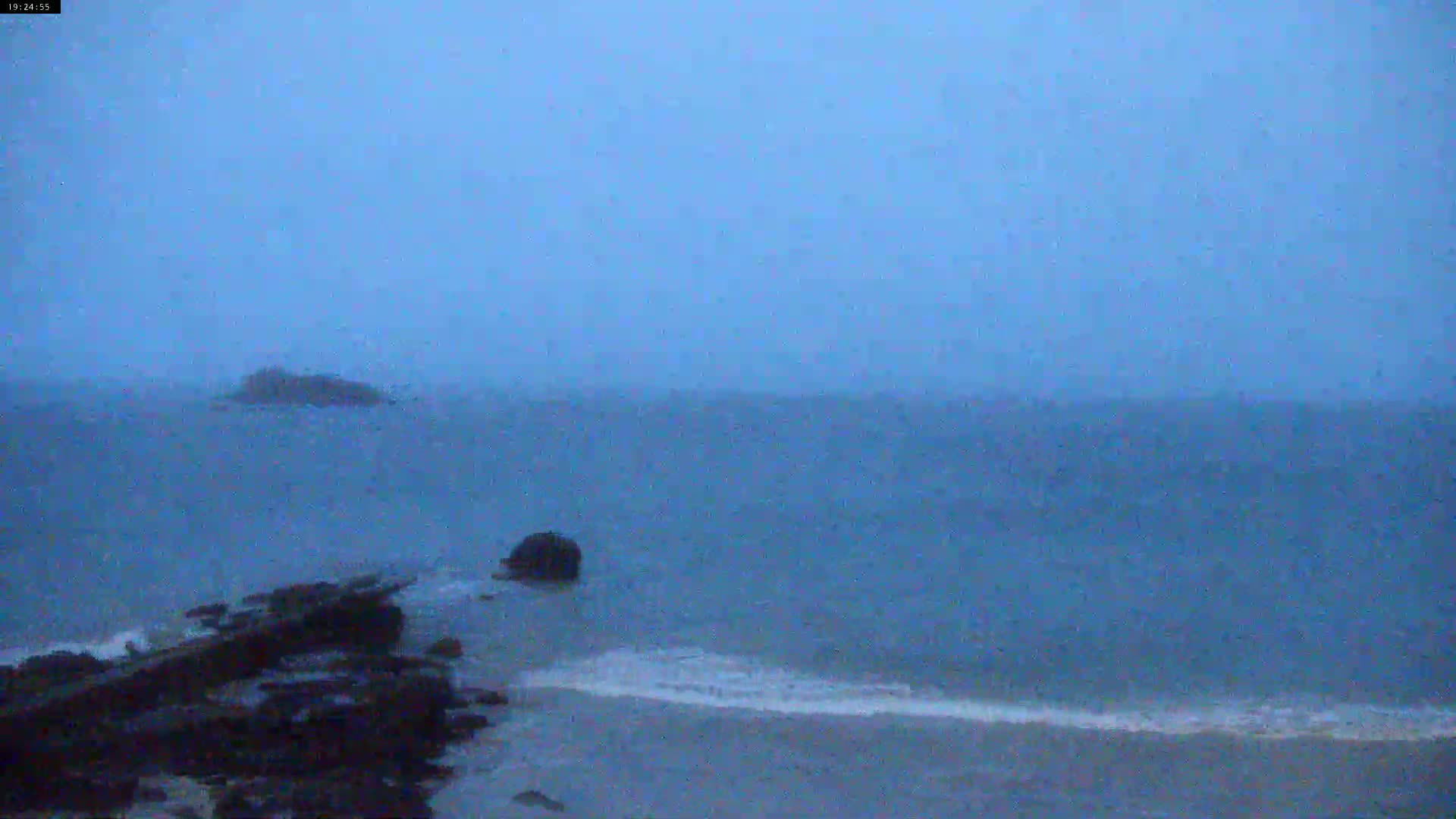 A rocky shoreline meets a dark, choppy sea under a hazy, overcast sky.
