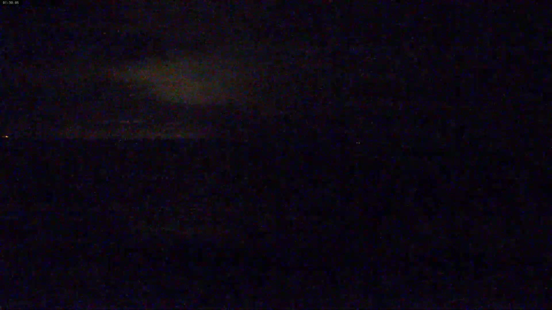 A dark, nighttime scene shows a mostly clear sky with faint clouds and a dark, indistinct landscape below.