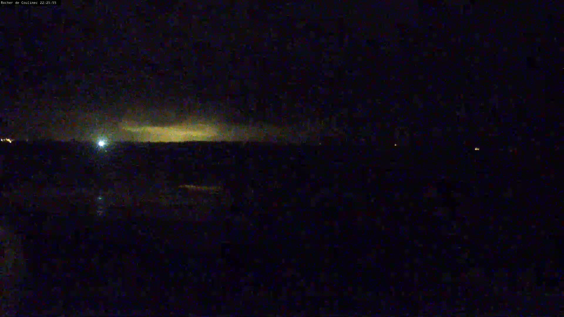 A dark, nighttime landscape is shown with a faint, yellowish glow on the horizon under a mostly clear sky.