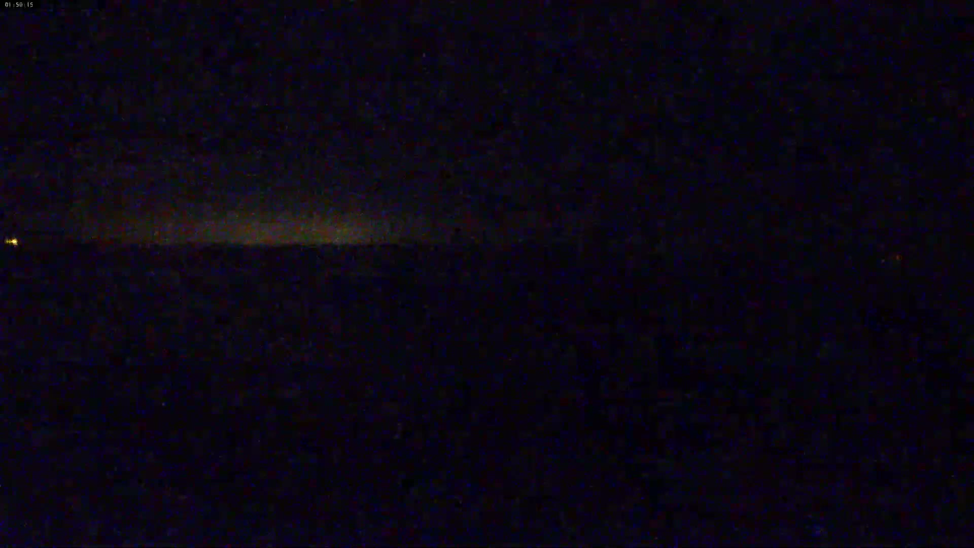 A dark, nighttime landscape is shown with a faint, horizontal glow on the horizon.