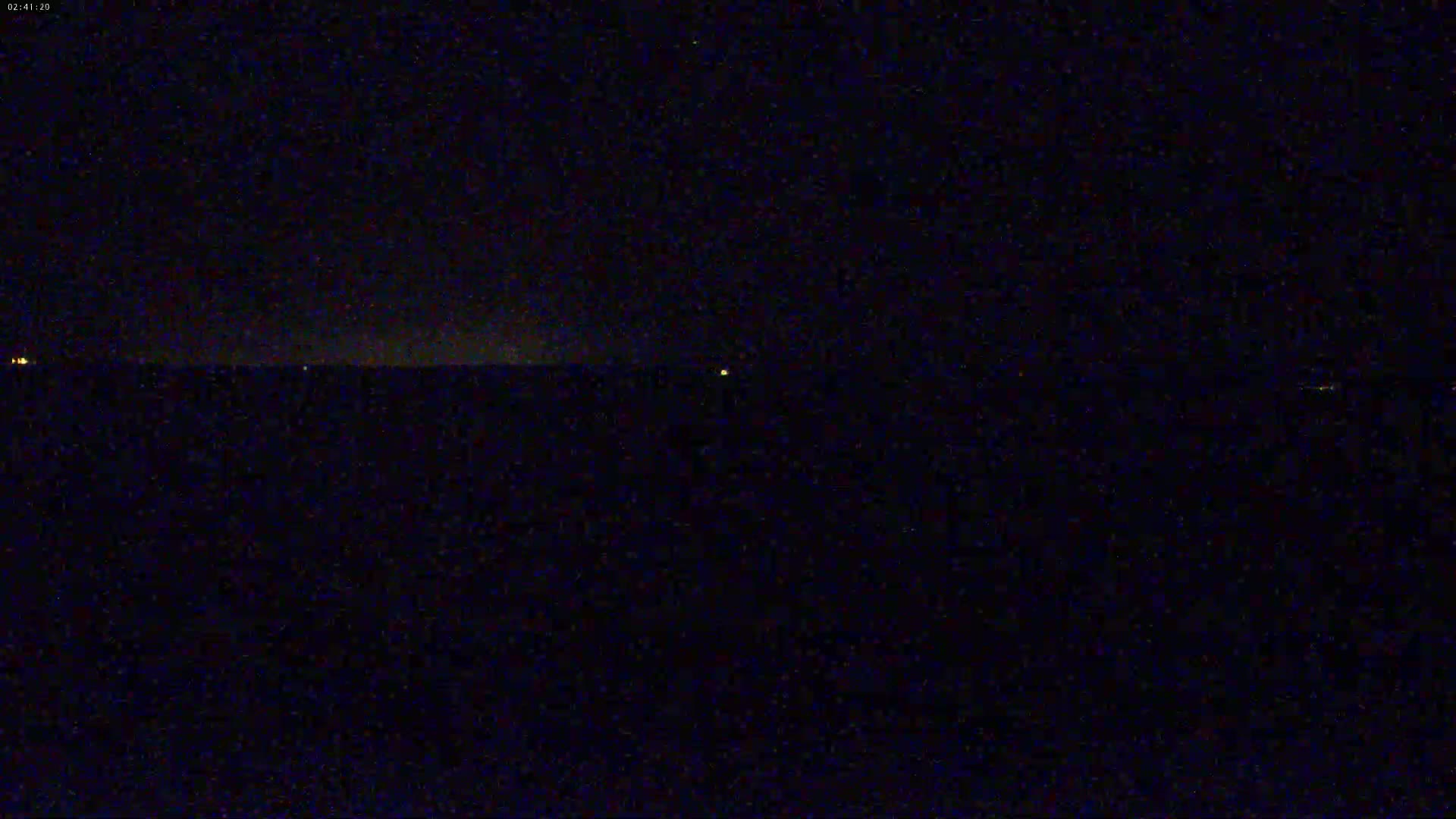A dark, nighttime scene shows a flat horizon line with a few faint, distant lights.