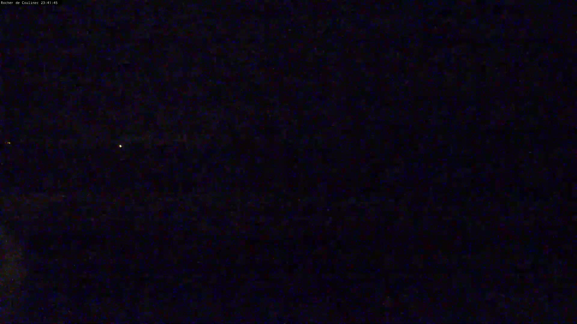 A dark, nighttime outdoor scene shows a few faint lights in the distance under a clear sky.