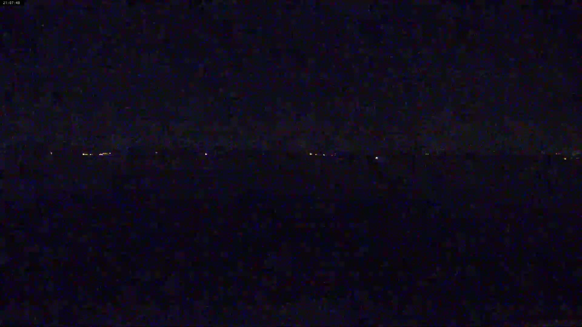 A dark, nighttime scene shows a distant line of faint lights on the horizon under a clear, starless sky.