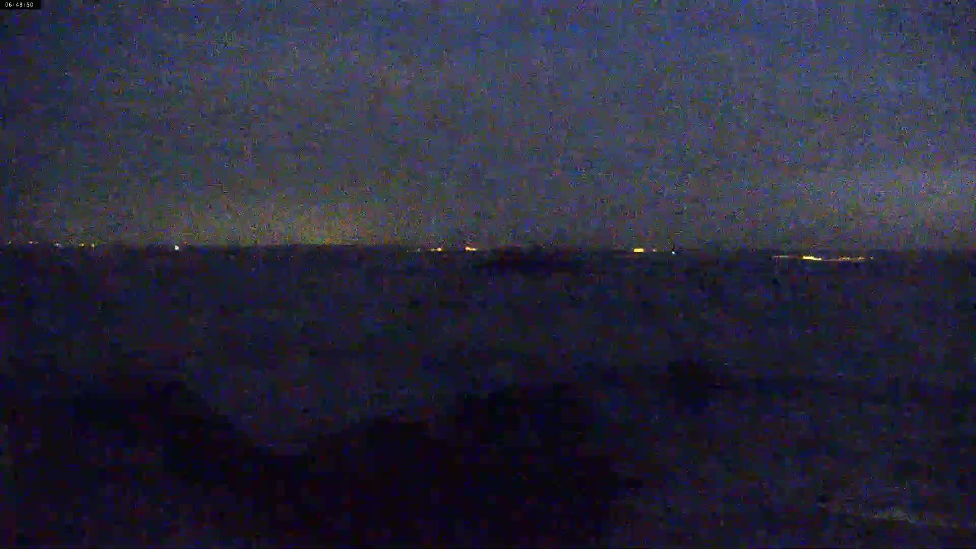 A dark, nighttime view shows a distant horizon with faint lights, possibly from a city, under a mostly clear sky.