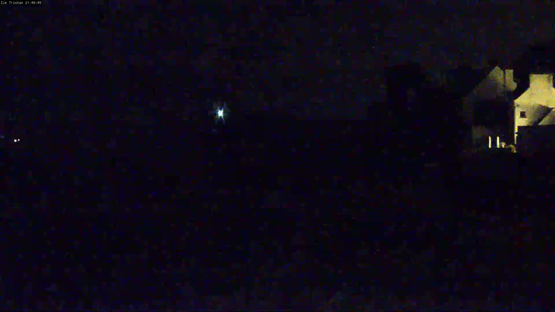 A dimly lit house is visible at night under a dark sky with a single, bright light source in the distance.
