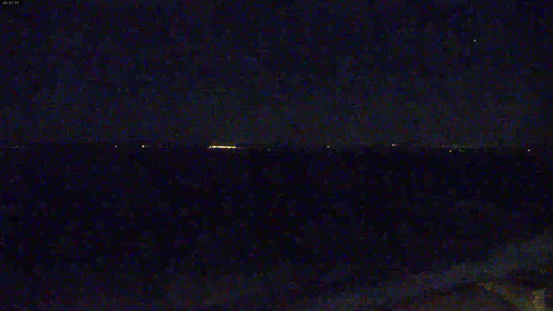 A dark, nighttime scene shows a distant, faintly lit horizon line under a clear, star-filled sky.