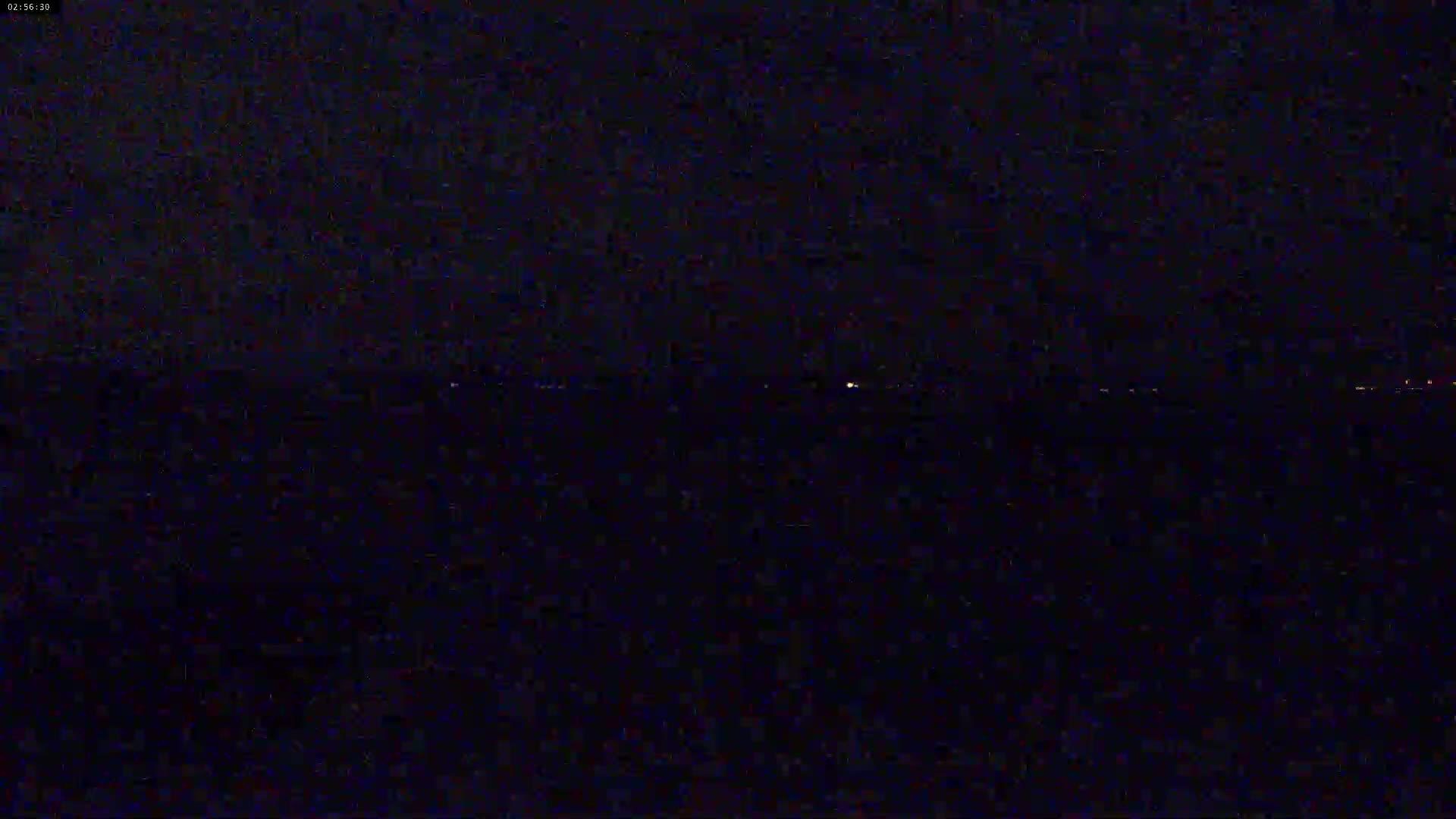 A dark, nighttime view of a body of water with a faint, distant line of lights on the horizon.